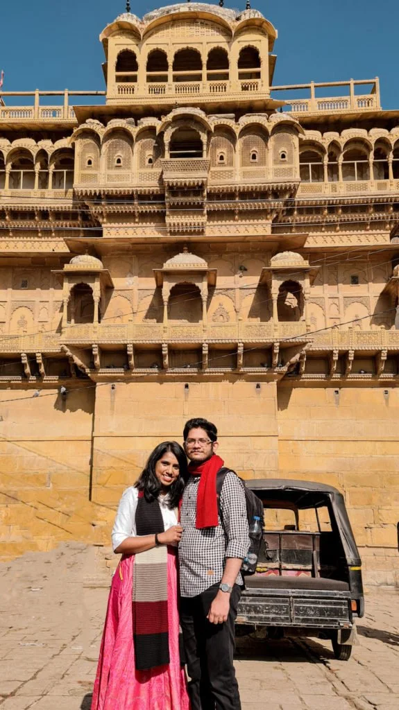 Roopesh and Kiki from RooKiExplorers posing in front of a palace inside an old fort in Jaisalmer.