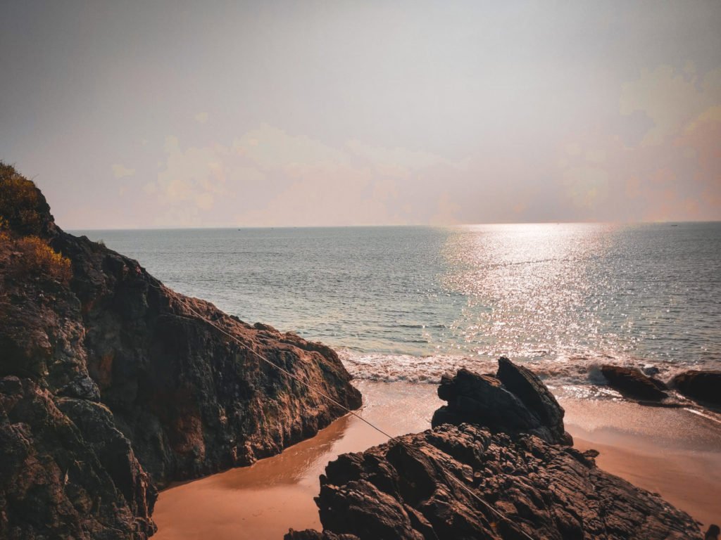 A beach in India with dark colored rocks in the shore.