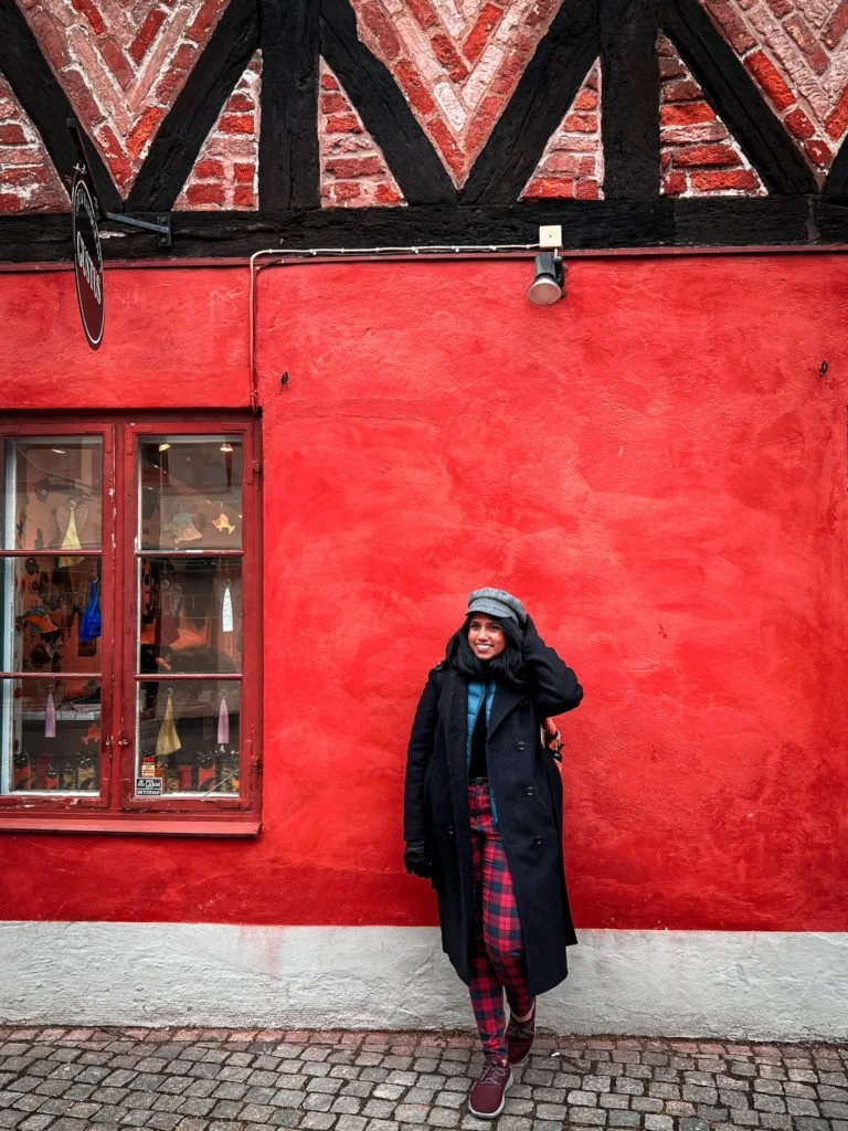 Kiki from RooKiExplorers posing in front of a building's red wall in Lilla Torg.