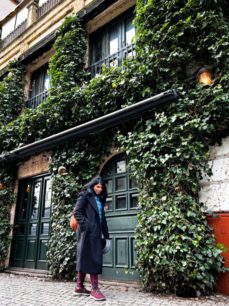 Kiki from RooKiExplorers walking near a building covered with creepers in Malmo.