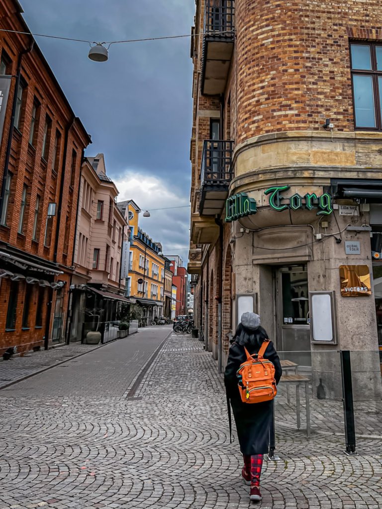 Kiki from RooKiExplorers walking towards the Lilla Torg neon sign.