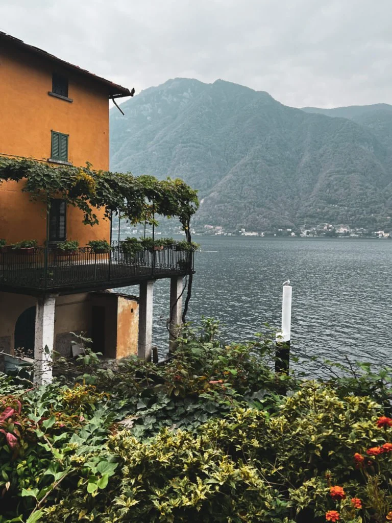A yellow building covered with vines and other plants near the dock of Nesso.