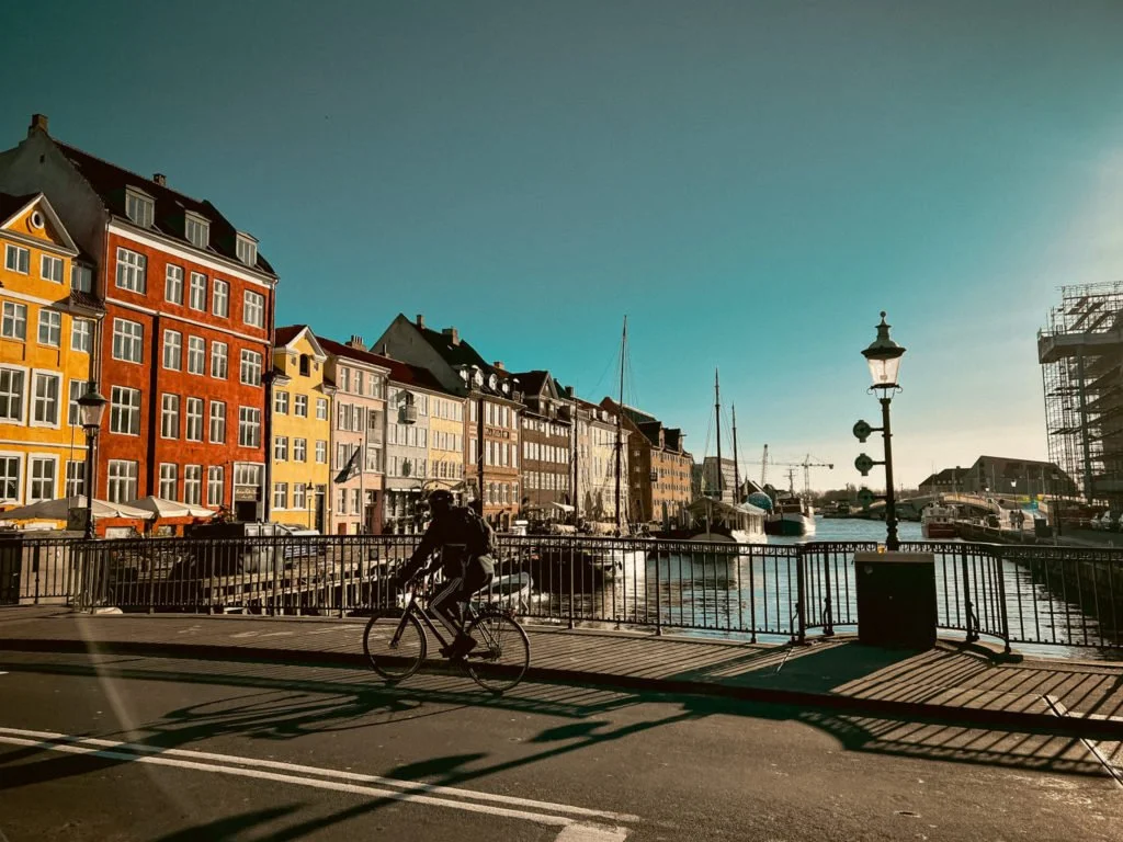 The buildings of Nyhavn with their cafes. A bike rider is riding a bike on a nearby bridge.