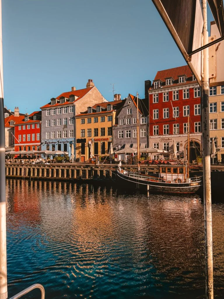 The buildings of Nyhavn with their cafes. A boat is docked in the canal.