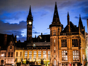 A medieval clock tower, a few medieval buildings, and a canal in Ghent during blue hour.