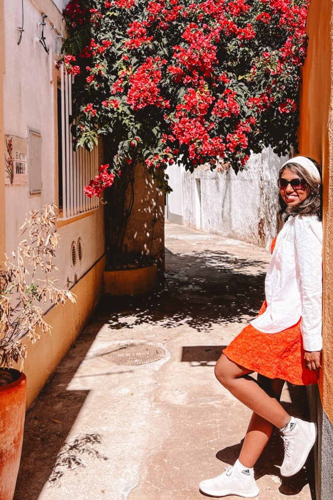 Kiki from RooKiExplorers posing in a street with big red bougainvillea tree in Ferragudo, Algarve.