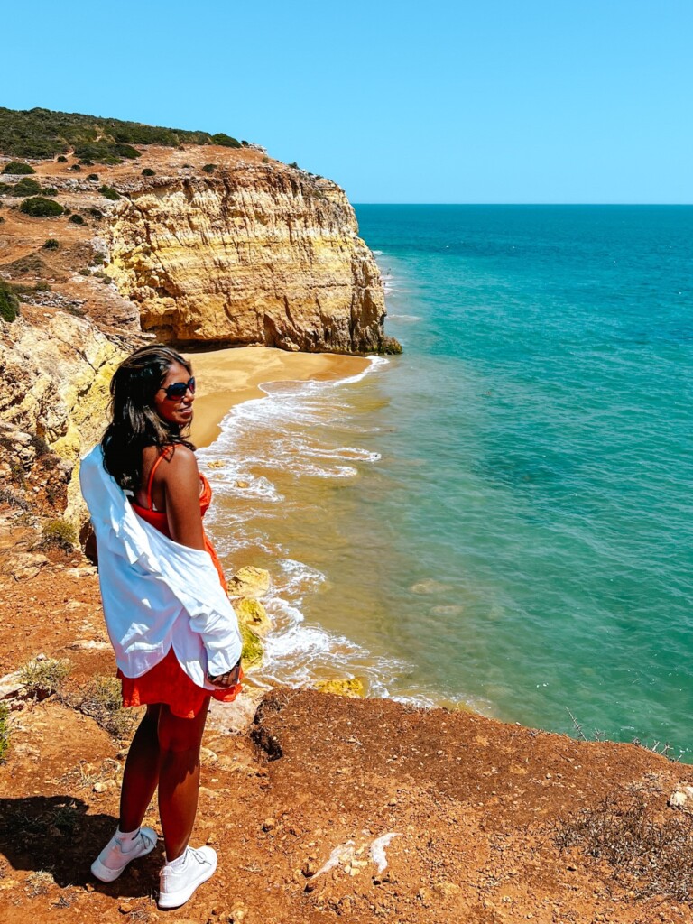 Kiki from RooKiExplorers posing near the edge of a cliff with Praia do Torrado in the background in Ferragudo, Algarve.