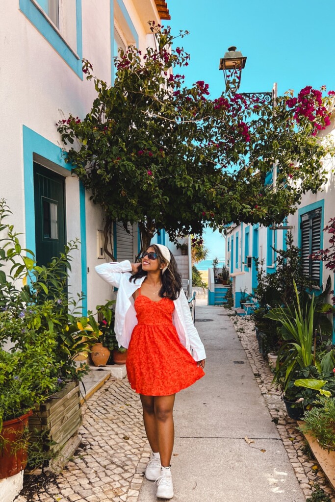 Kiki from RooKiExplorers strolling in a street with a bougainvillea tree and blue and white colored houses in Ferragudo, Algarve.