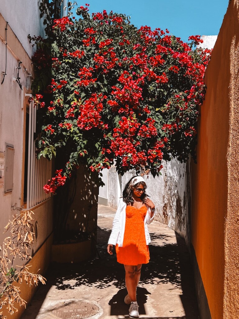 Kiki from RooKiExplorers strolling in a street with big red bougainvillea tree in Ferragudo, Algarve.