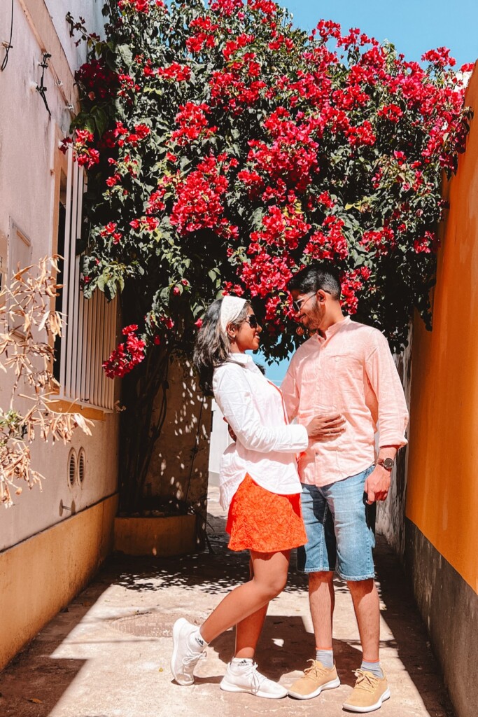 Roopesh and Kiki from RooKiExplorers posing in a street with big red bougainvillea tree in Ferragudo, Algarve.