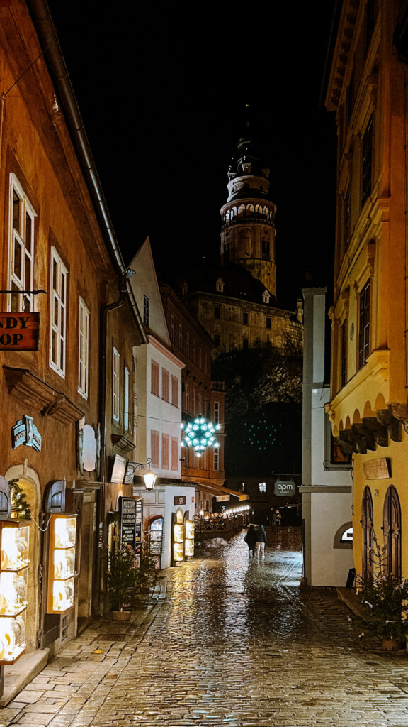 A road in Český Krumlov with Christmas lights and Český Krumlov's castle in the background.
